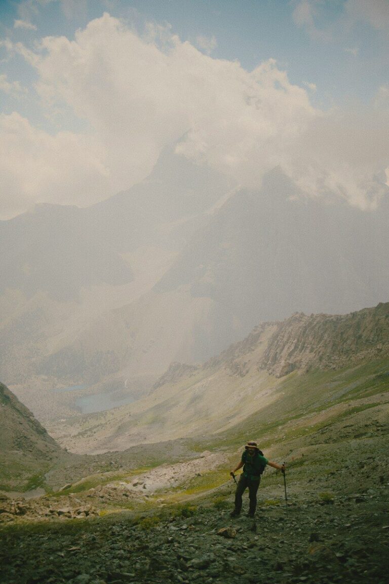 A hiker with trekking poles on a rocky mountain slope above a valley